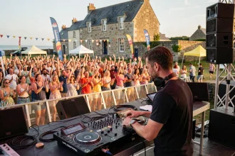 DJ professionnel en pleine performance sur scène lors d'un festival estival en Bretagne, avec une foule animée et une architecture bretonne en arrière-plan